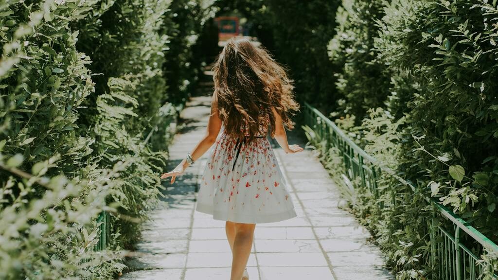 Photography of Woman in White and Red Floral Midi Dress Walking on Pathway